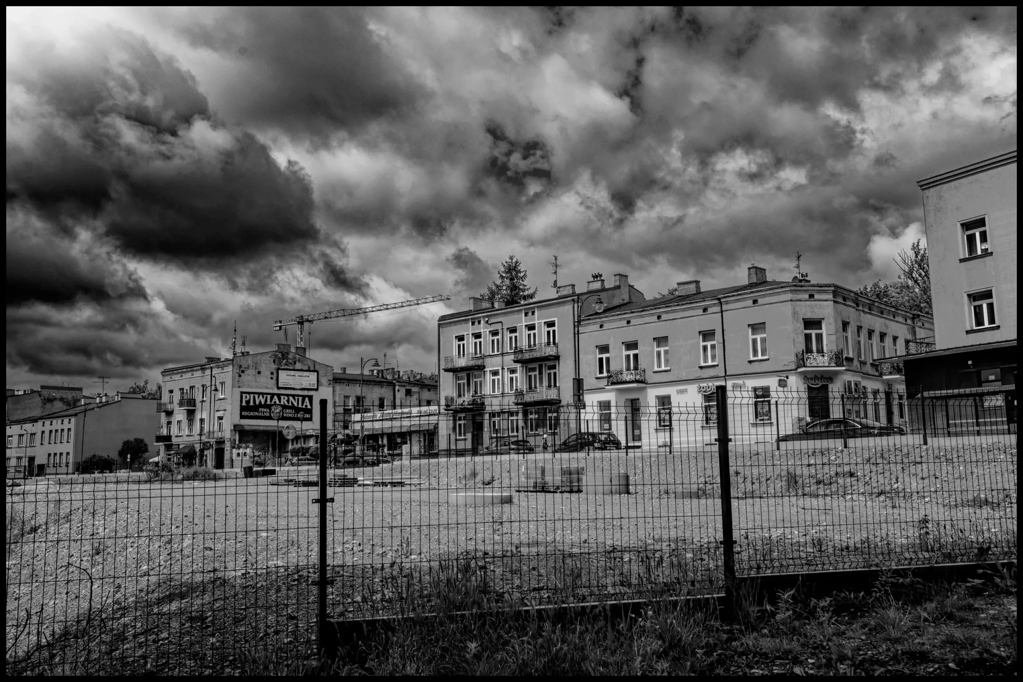 A fenced lot in Częstochowa under stormy skies. The past is never far.